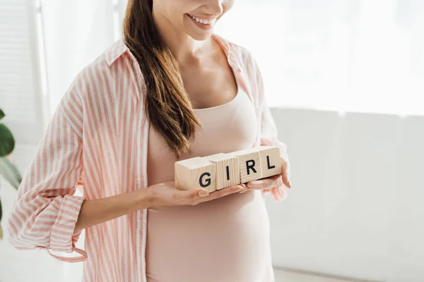 Vista recortada de la mujer embarazada sonriente sosteniendo bloques de madera con palabra - foto de stock