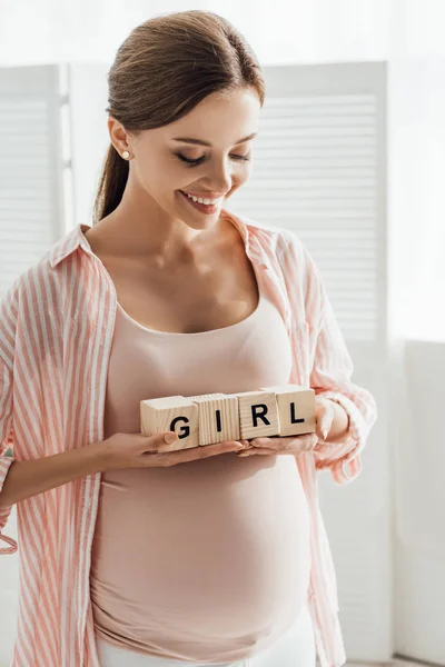 Mujer embarazada sonriente sosteniendo bloques de madera con palabra - foto de stock
