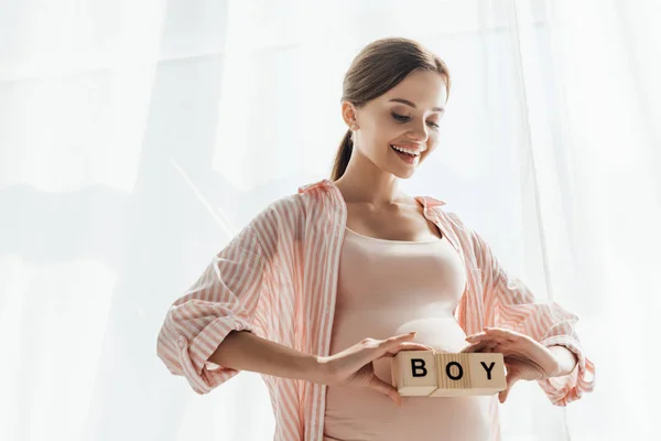 Mujer embarazada sonriente sosteniendo bloques de madera con word boy - foto de stock