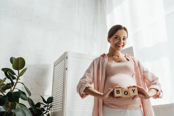 Souriant femme enceinte tenant des blocs de bois avec mot garçon — Photo de stock