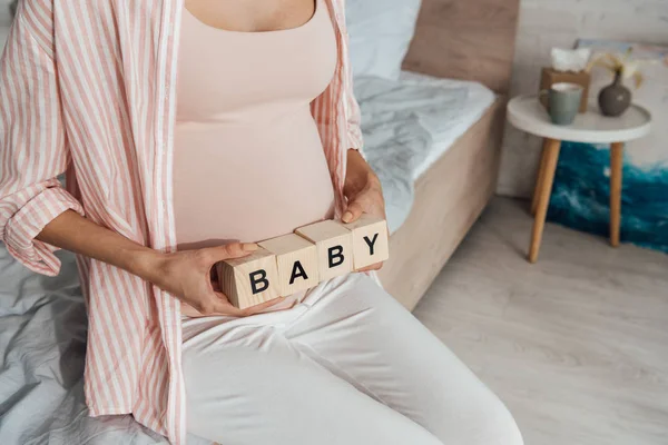 Vista recortada de la mujer embarazada sosteniendo bloques de madera con palabra bebé - foto de stock
