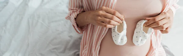 Panoramic shot of pregnant woman holding baby shoes — Stock Photo