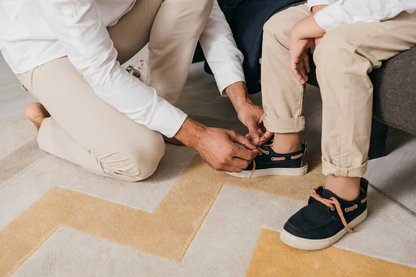 Vista ritagliata del padre legatura lacci delle scarpe per il figlio a casa — Foto stock