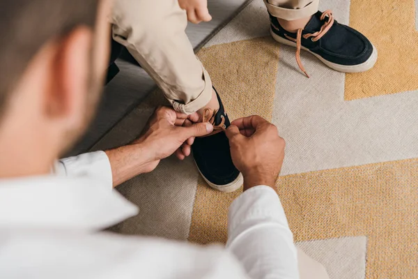 Cropped view of father tying shoelaces for son at home — Stock Photo