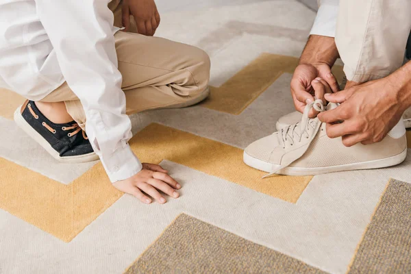 Visión parcial de padre enseñando hijo a atar cordones en casa - foto de stock