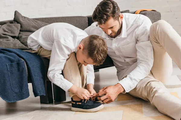 Padre enseñando hijo a atar cordones en casa - foto de stock