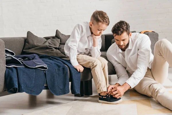 Padre sentado en la alfombra y atando cordones para el hijo - foto de stock