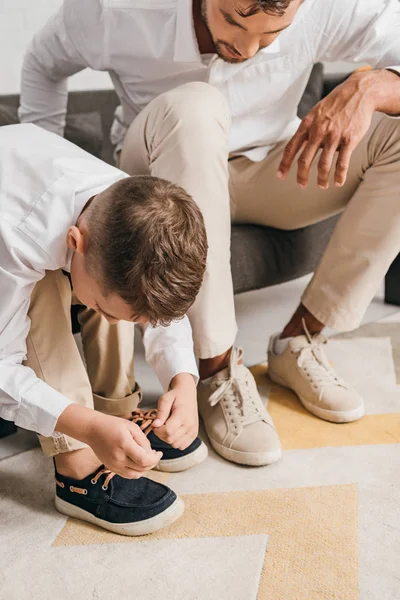 Vista recortada de padre enseñando hijo a atar cordones de zapatos en casa - foto de stock