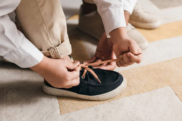 Visión parcial de padre enseñando hijo a atar cordones en casa - foto de stock