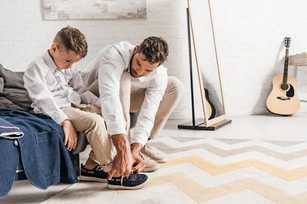 Padre enseñando hijo a atar cordones en casa - foto de stock