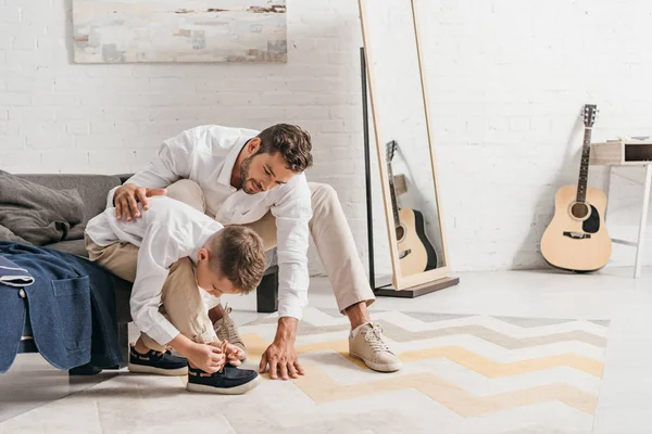 Padre enseñando hijo a atar cordones en casa - foto de stock