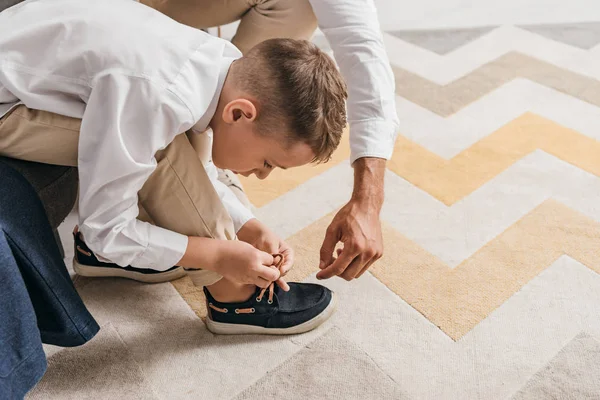 Частичный взгляд отца, обучающего сына завязыванию шнурков дома — стоковое фото