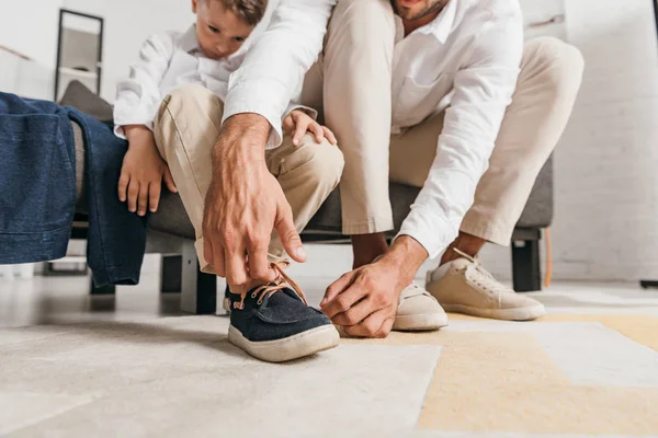 Vue partielle du père enseignant le fils à attacher des lacets à la maison — Photo de stock