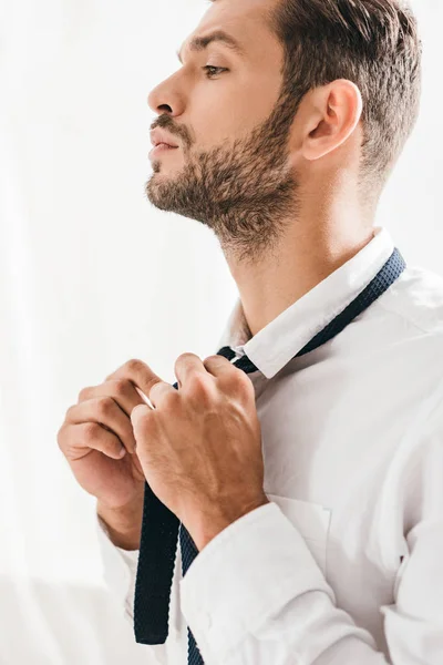 Serious bearded man in white shirt tying tie — Stock Photo