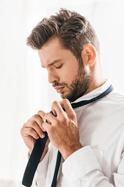 Serious bearded man in white shirt tying tie — Stock Photo