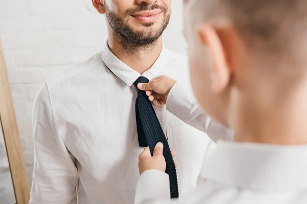 Corte vista do filho na camisa branca ajudando o pai com gravata em casa — Fotografia de Stock