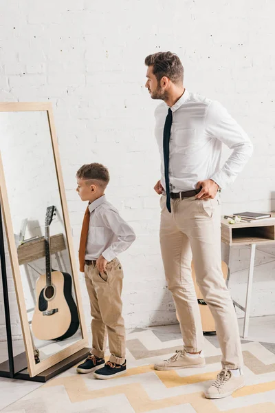 Visão de comprimento total do filho e do pai em desgaste formal de pé perto do espelho — Fotografia de Stock