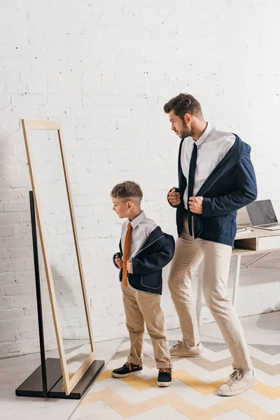 Vista de longitud completa de padre y padre en ropa formal de pie cerca de la ventana en casa - foto de stock