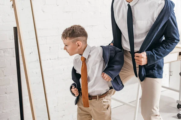 Vista parziale del figlio e del padre in abito formale in piedi vicino allo specchio a casa — Foto stock