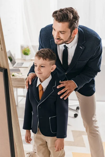 Padre seguro de sí mismo y su hijo en ropa formal en casa - foto de stock