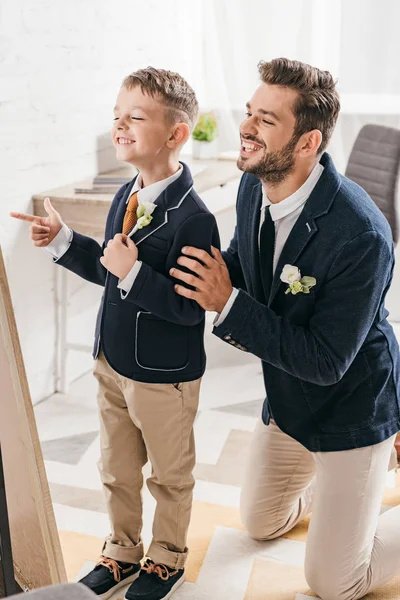 Smiling dad and son in jackets with boutonnieres at home — Stock Photo