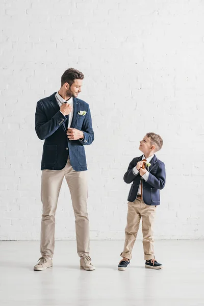 Ganzheitliche Ansicht von Vater und Sohn in Jacken mit Boutonnieres, die sich gegenseitig anschauen — Stockfoto
