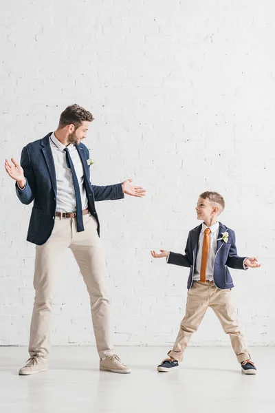 Visão de comprimento total de pai e filho em jaquetas com boutonnieres olhando um para o outro — Fotografia de Stock