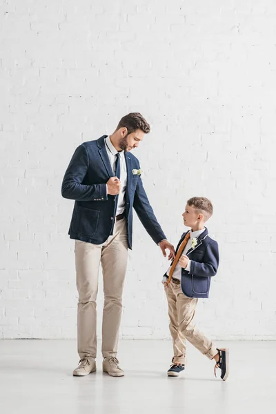 Vista completa de padre e hijo en chaquetas con boutonnieres mirándose - foto de stock