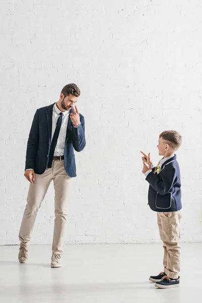 Visão de comprimento total de pai e filho em jaquetas com boutonnieres olhando um para o outro — Fotografia de Stock