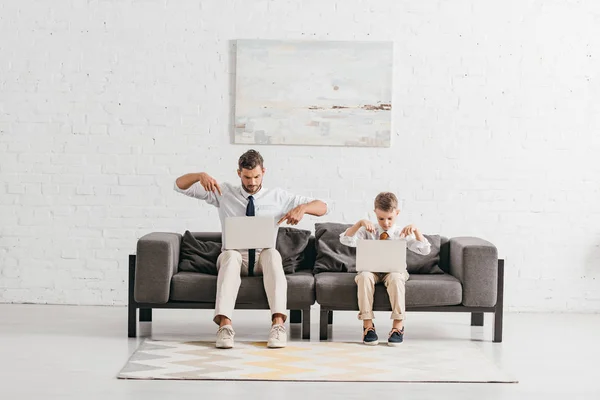 Pai e filho em desgaste formal usando laptops enquanto sentado no sofá — Fotografia de Stock