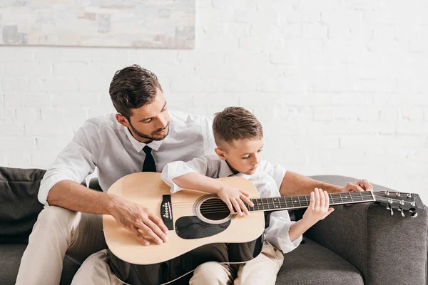 Pai ensinando filho a tocar guitarra acústica em casa — Fotografia de Stock