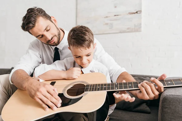Папа учит сына играть на акустической гитаре дома — стоковое фото