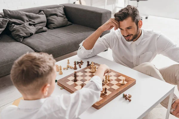 Папа и сын играют вместе в шахматы дома — стоковое фото