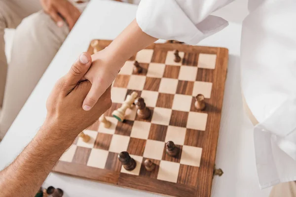 Partial view of dad and son shaking hands over chessboard — Stock Photo