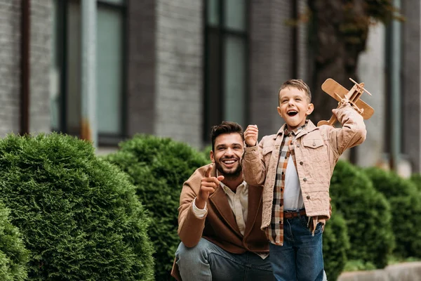 Happy bearded father and son with toy plane smiling on street — Stock Photo