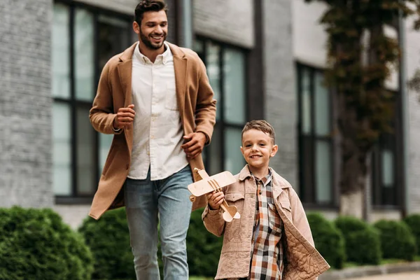 Papa souriant en manteau et fils avec avion jouet courant dans la rue — Photo de stock