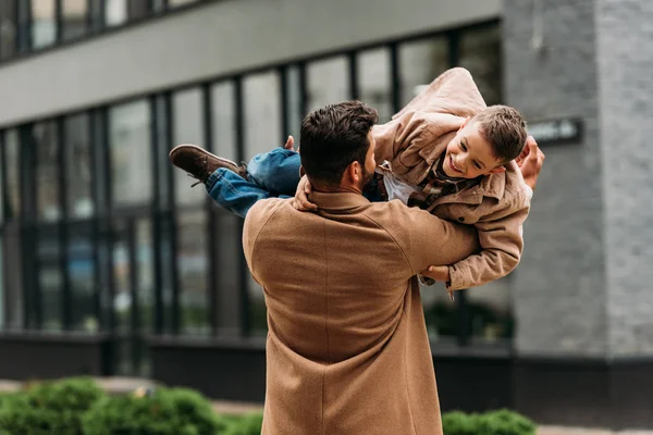 Back view of father in coat holding smiling son on street — Stock Photo