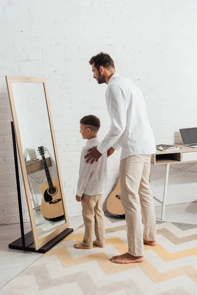 Полный вид босых отца и сына, стоящих у зеркала — стоковое фото