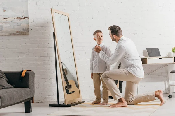 Padre ayudando a su hijo a vestirse cerca del espejo - foto de stock