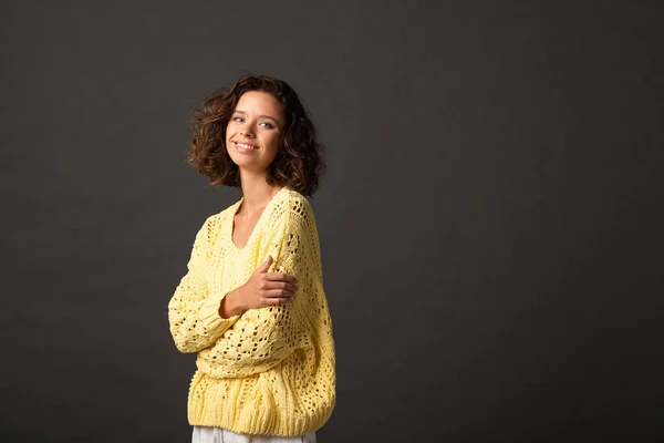 Femme bouclée souriante en pull tricoté jaune sur fond noir — Photo de stock