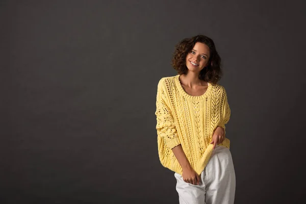 Smiling curly woman in yellow knitted sweater on black background — Stock Photo