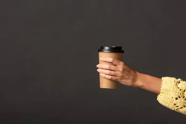 Vista cortada de mulher em camisola de malha amarela segurando café para ir no fundo preto — Fotografia de Stock