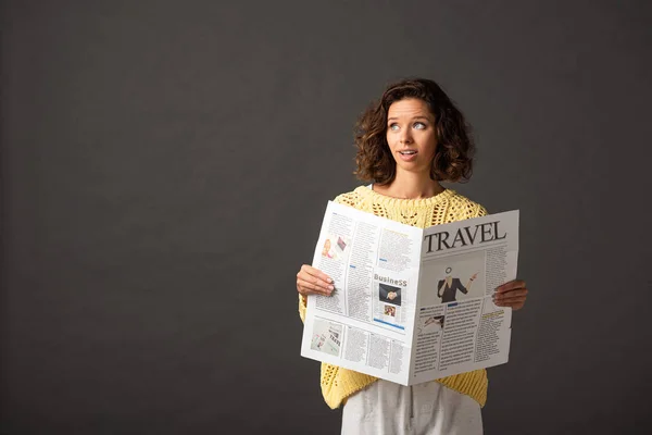 Dreamy curly woman in yellow knitted sweater holding travel newspaper on black background — Stock Photo