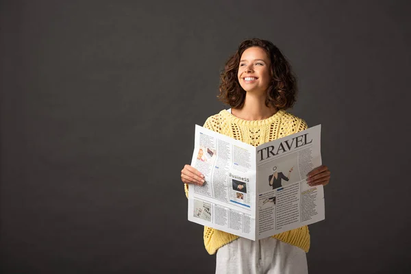 Femme bouclée souriante en chandail tricoté jaune tenant journal de voyage sur fond noir — Photo de stock