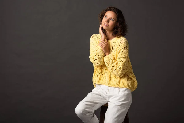 Dreamy curly woman in yellow knitted sweater looking away on black background — Stock Photo