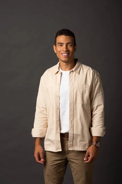 Sonriente guapo mixto raza hombre en beige camisa en negro fondo - foto de stock