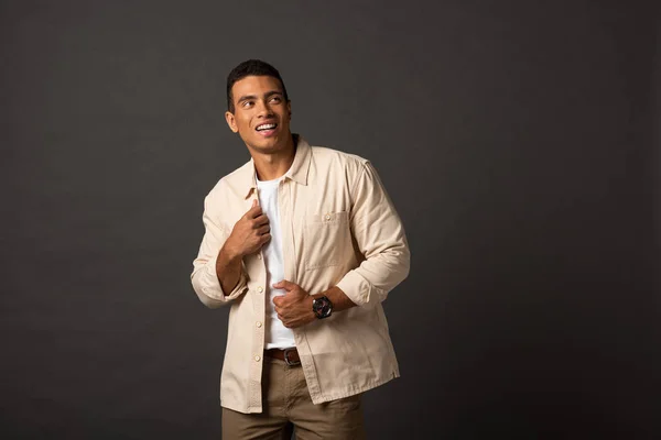 Smiling handsome mixed race man in beige shirt looking away on black background — Stock Photo