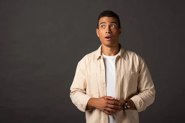 Shocked handsome mixed race man in beige shirt looking away on black background — Stock Photo