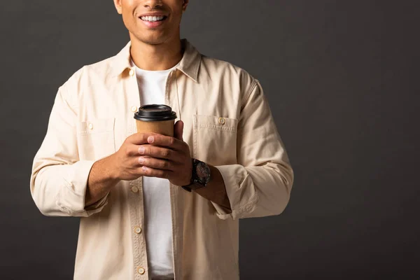 Vista parcial del hombre de raza mixta en camisa beige sosteniendo café para ir sobre fondo negro - foto de stock