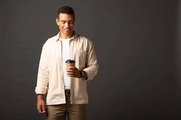 Heureux beau mixte homme en chemise beige tenant café pour aller sur fond noir — Photo de stock